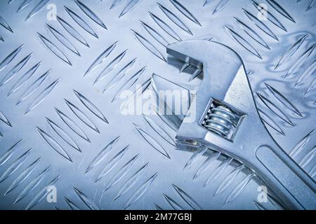 Affenschlüssel aus Edelstahl auf gewelltem Metallhintergrund, Baukonzept Draufsicht. Stockfoto