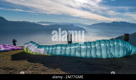 Männer auf einem Grashang bereiten den Gleitschirmflug von Vetriolo Terme - Provinz Trient - Trentino Alto Adige - Paragliding-Schule - Italien vor Stockfoto