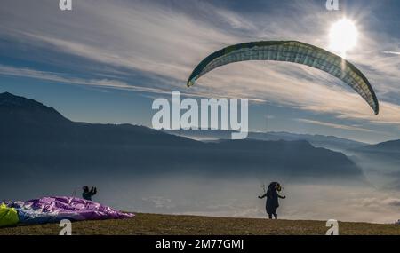 Männer auf einer grasbewachsenen Hanglage bereiten den Gleitschirmflug von Vetriolo Terme, Provinz Trient - Trentino Alto Adige - Paragliding-Schule - Italien vor Stockfoto