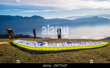 Männer auf einer grasbewachsenen Hanglage bereiten den Gleitschirmflug von Vetriolo Terme, Provinz Trient - Trentino Alto Adige - Paragliding-Schule - Italien vor Stockfoto