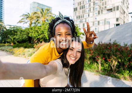 Zwei multiethnische weibliche Freunde, die sich mit dem Mobiltelefon im Freien fotografieren Stockfoto