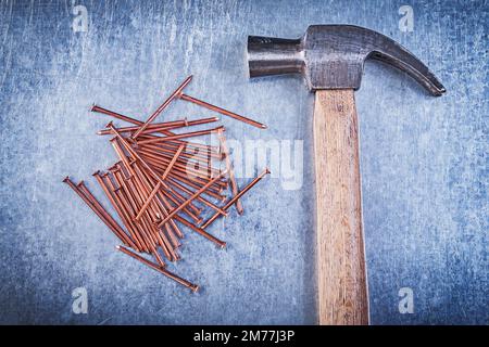 Vintage-Klauenhammer, Kupfernägel auf metallischem Hintergrund direkt darüber. Stockfoto