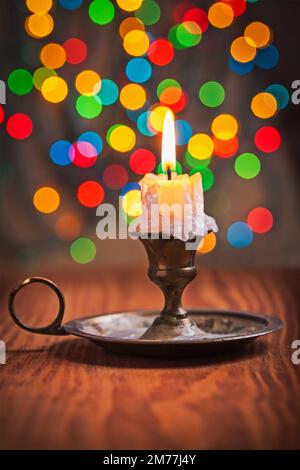 Alte Kerze im Kerzenhalter auf Holzbrett und Hintergrund mit Bokeh Stockfoto