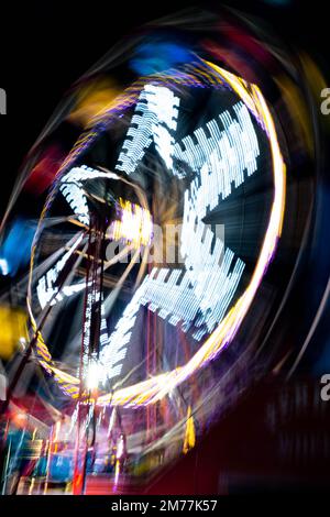 Abstrakte Bewegungsunschärfe von sich drehenden Fahrgeschäften auf dem Festgelände mit farbenfrohen Lichtwegen bei Nacht Stockfoto