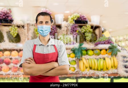 Geschäftseigentümer, der mit einer roten Schürze in einem Obstgeschäft arbeitet und eine Gesichtsmaske trägt, um das Coronavirus zu vermeiden - Pandemie-Lifestyle-Konzepte und Kopierraum. Stockfoto