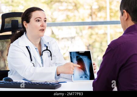 Aufnahme einer jungen Ärztin mit einem digitalen Tablet während einer Sprechstunde mit einem reifen Mann Stockfoto