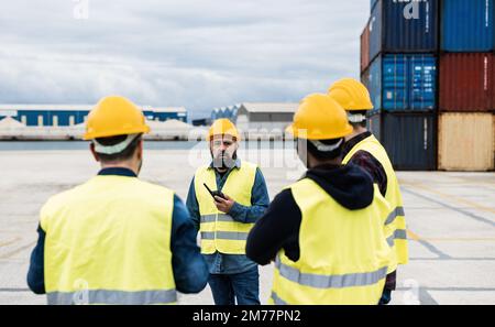 Arbeiter, die Transportbehälter am industriellen Hafen im Freien kontrollieren – Fokus auf das Center man Face Stockfoto