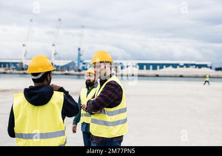 Arbeiter, die Schiffscontainer im Industriehafen im Freien kontrollieren - Fokus auf das rechte Menschengesicht Stockfoto