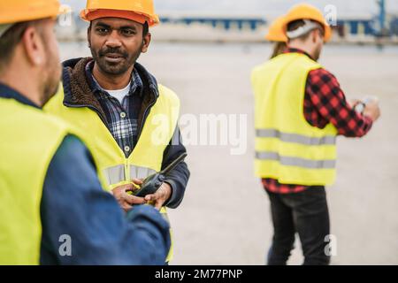 Arbeiter, die Schiffscontainer im Industriehafen im Freien kontrollieren - Fokus auf das indische Männergesicht Stockfoto