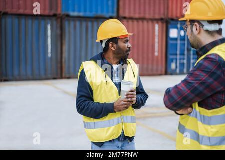 Arbeiter, die Schiffscontainer im Industriehafen im Freien kontrollieren - Fokus auf das indische Männergesicht Stockfoto