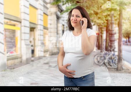 Aufnahme einer schmerzhaften schwangeren Frau, die in der Stadt medizinische Hilfe ruft Stockfoto