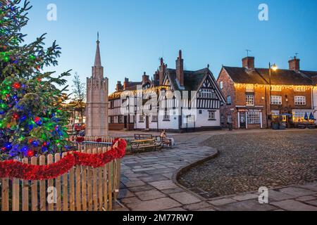 Der kopfsteingepflasterte Marktplatz in Sandbach in Cheshire mit seinem Weihnachtsbaum und Lichtern und dem zenotaph war Memorial und schwarz-weiß Coaching Inn Stockfoto