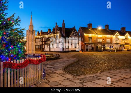 Der kopfsteingepflasterte Marktplatz in Sandbach in Cheshire mit seinem Weihnachtsbaum und Lichtern und dem zenotaph war Memorial und schwarz-weiß Coaching Inn Stockfoto