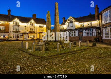 Der mit Flutlicht beleuchtete alte kopfsteingepflasterte Marktplatz in der Cheshire Marktstadt Sandbach mit den sächsischen Kreuzen und zwei alten Trainerhäusern in der Nacht Stockfoto