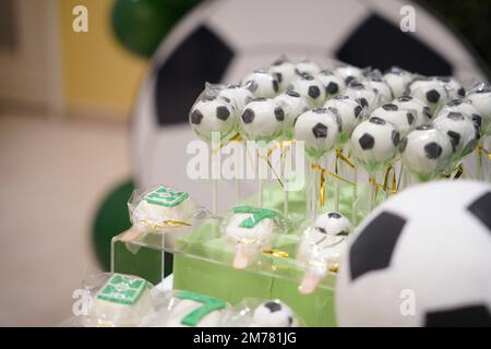 Fußball- oder Fußball-Geburtstagskunzentisch mit grünen Keksen und kleinen Fußballbällen, Pop-Kuchen auf einem Geburtstagsbanner-Hintergrund. Stockfoto