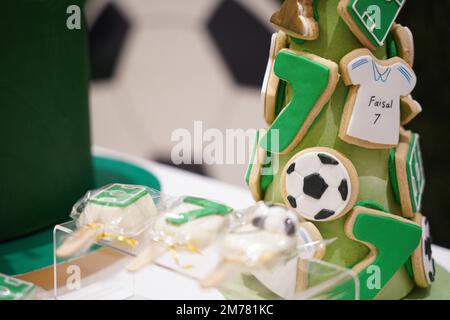 Fußball- oder Fußball-Geburtstagskunzentisch mit grünen Keksen und kleinen Fußballbällen, Pop-Kuchen auf einem Geburtstagsbanner-Hintergrund. Stockfoto