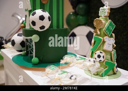 Fußball- oder Fußball-Geburtstagskunzentisch mit grünen Keksen und kleinen Fußballbällen, Pop-Kuchen auf einem Geburtstagsbanner-Hintergrund. Stockfoto