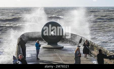 Brighton UK 8. Januar 2023 - Besucher werden nass, wenn sie beobachten, wie die Wellen am Brighton Beach und am Meer an der berühmten Donut-Skulptur einschlagen, während Stürme die Südküste heute mit einer Mischung aus starkem Wind, Sonnenschein und Regen treffen : Credit Simon Dack / Alamy Live News Stockfoto