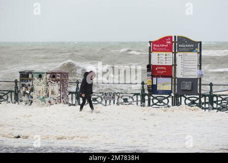 Brighton & Hove, East Sussex. 7. Januar 2023 Wetter in Großbritannien. Die Menschen und ihre Hunde kämpfen in starken 40mph-Winden und waten durch eine Promenade, die von den stürzenden Wellen bedeckt ist und bei Flut an der Küste von Hove liegt. Kredit: Francesca Moore/Alamy Live News Stockfoto