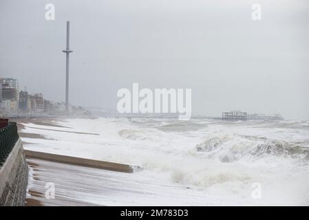 Brighton & Hove, East Sussex. 7. Januar 2023 Wetter in Großbritannien. Die Menschen und ihre Hunde kämpfen in starken 40mph-Winden und waten durch eine Promenade, die von den stürzenden Wellen bedeckt ist und bei Flut an der Küste von Hove liegt. Kredit: Francesca Moore/Alamy Live News Stockfoto