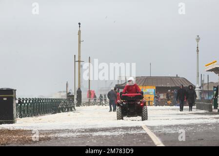 Brighton & Hove, East Sussex. 7. Januar 2023 Wetter in Großbritannien. Die Menschen und ihre Hunde kämpfen in starken 40mph-Winden und waten durch eine Promenade, die von den stürzenden Wellen bedeckt ist und bei Flut an der Küste von Hove liegt. Kredit: Francesca Moore/Alamy Live News Stockfoto