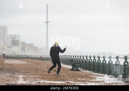 Brighton & Hove, East Sussex. 7. Januar 2023 Wetter in Großbritannien. Die Menschen und ihre Hunde kämpfen in starken 40mph-Winden und waten durch eine Promenade, die von den stürzenden Wellen bedeckt ist und bei Flut an der Küste von Hove liegt. Kredit: Francesca Moore/Alamy Live News Stockfoto