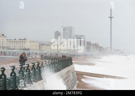 Brighton & Hove, East Sussex. 7. Januar 2023 Wetter in Großbritannien. Die Menschen und ihre Hunde kämpfen in starken 40mph-Winden und waten durch eine Promenade, die von den stürzenden Wellen bedeckt ist und bei Flut an der Küste von Hove liegt. Kredit: Francesca Moore/Alamy Live News Stockfoto