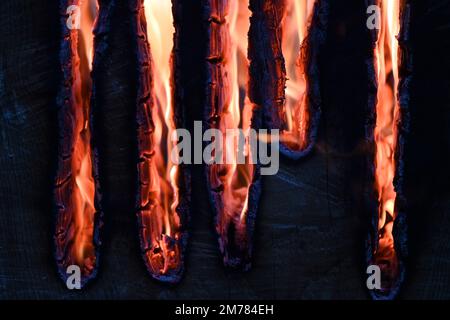 Nahaufnahme leuchtender orangener Flammen, die in Dunkelheit verkohlte Holzlatten verzehren Stockfoto