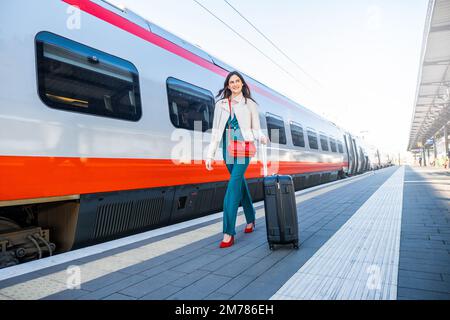 Porträt einer Geschäftsfrau, die mit Handgepäck in einem Bahnhof oder Flughafen zum Boarding Gate geht Stockfoto