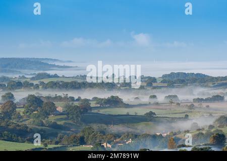 Wolkeninversion an einem späten Sommermorgen über dem Lune Valley in Lancashire, mit Blick über Burton in Lonsdale in Richtung Lancaster von oberhalb von Ingleton. U Stockfoto