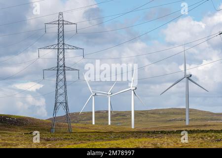 Stromleitungen marschieren über ein schottisches Moor, mit Windturbinen dahinter. Highlands, Schottland, Großbritannien. Stockfoto