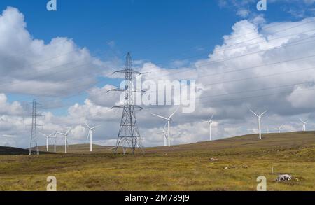 Stromleitungen marschieren über ein schottisches Moor, mit Windturbinen dahinter. Highlands, Schottland, Großbritannien. Stockfoto