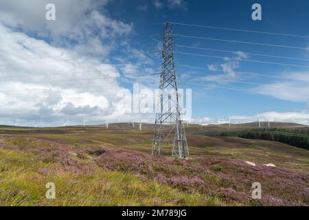 Stromleitungen marschieren über ein schottisches Moor, mit Windturbinen dahinter. Highlands, Schottland, Großbritannien. Stockfoto