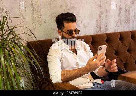 Der Unternehmer nutzt das Handy. Junger, gutaussehender Geschäftsmann, arabischer moslem, im Business Center. Technologien und Geschäftskonzept. Stockfoto