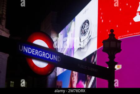 Beleuchtetes Schild für die Londoner U-Bahn, U-Bahn oder U-Bahn vor den Anzeigebildschirmen in Piccadilly Circus, London, Großbritannien Stockfoto