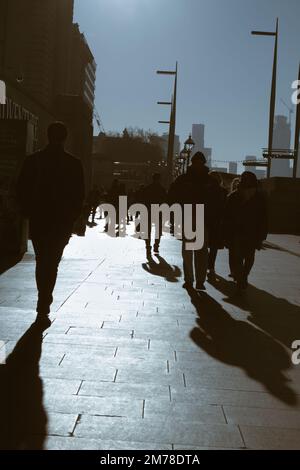 Silhouette einer Menschenmenge, die entlang der South Bank an der Westminster Bridge Backlit by the Sun im Winter, London, Großbritannien, spaziert Stockfoto