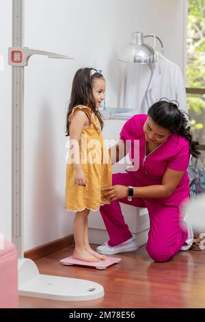 Kinderärztin, die ein Mädchen auf einer Bodenwaage wiegt, in ihrem Büro. Stockfoto