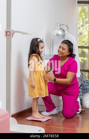 Kinderärztin, die ein Mädchen auf einer Bodenwaage wiegt, in ihrem Büro. Stockfoto