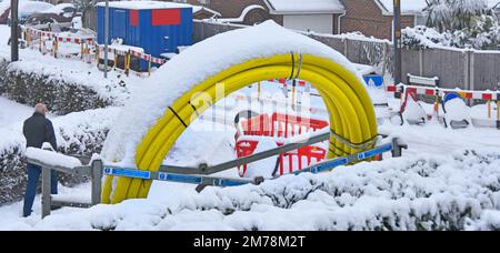 Winter Schneefall verzögert die Straßenarbeiten von Lohnunternehmern in der Straße eines Wohndorfes, um alte Gasleitungen aus Stahl zu ersetzen, indem neue gelbe Rohrleitungen eingeführt werden, die mit Wohnhäusern in Großbritannien verbunden sind Stockfoto