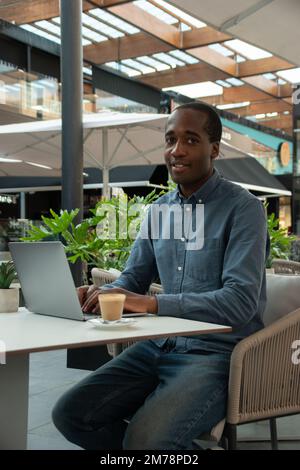 Ein junger afrikanischer Geschäftsmann mit seinem Laptop macht eine Kaffeepause Stockfoto
