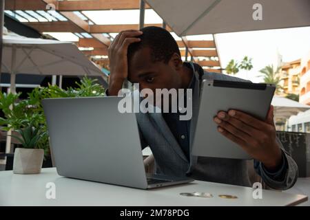 Ein enttäuschter Händler erhält schlechte Nachrichten, wenn er den Markt über sein Tablet und sein Notebook überwacht Stockfoto