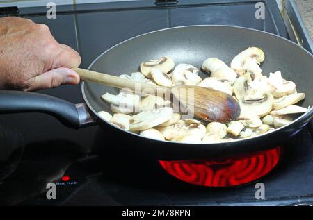 Ich koche Pilze in einer Pfanne. Mit einem Holzlöffel die in Scheiben geschnittenen Pilze umrühren. Stockfoto