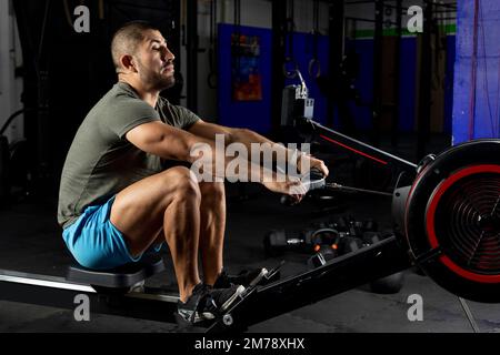 Ein Mann in Sportbekleidung rudert auf einer Maschine im Fitnessstudio Stockfoto