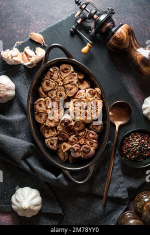 Geröstete Knoblauchknollen, frisch aus dem Ofen, vor dunklem Hintergrund. Stockfoto