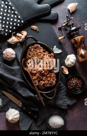 Gerösteter Knoblauch, frisch aus dem Ofen, mit rohen Knoblauchknollen und Zehen rundherum Stockfoto