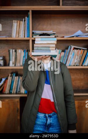 Eine Frau hält einen Stapel Bücher vor einem Regal mit gespendeten Büchern, die von den Interessierten gelesen werden sollen. Wiederverwendung von Büchern durch Antiquitätengeschäfte. Stockfoto