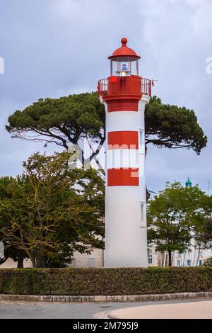 Ein hoher, weiß-roter Leuchtturm befindet sich in der malerischen Hafenstadt La Rochelle in Frankreich. Der Leuchtturm ist von Bäumen umgeben Stockfoto