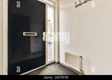Ein leerer Raum mit einer schwarzen Tür und weißen Wänden, es gibt ein kleines Fenster auf der rechten Seite Stockfoto