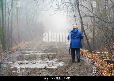 Eine ältere Frau geht in die neblige Ferne auf einer schmutzigen Straße Stockfoto