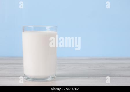 Das Glas voller Milch auf einem Holztisch. Ein Glas frische weiße Milch auf blauem Hintergrund in der Küche. Stockfoto
